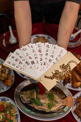 Lunar New Year flat lay of two hands holding a menu with a tiger etched into wood above traditional Chinese food and on a table top.