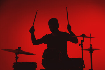 Silhouette of a young man playing drums on a red background