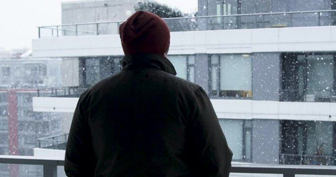 Slow-motion stock footage of a man enjoys the snow from his apartment balcony during a snowfall blizzard in Vancouver, Canada