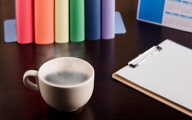 cup of coffee or tea with hot steam, books with lgtbi flag colors, notebook on the desk.