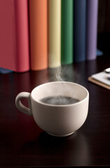 cup of coffee or tea with hot steam, books with lgtbi flag colors, on the desk.