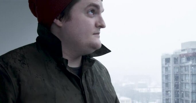 Slow-motion stock footage of a man enjoys the snow from his apartment balcony during a snowfall blizzard in Vancouver, Canada