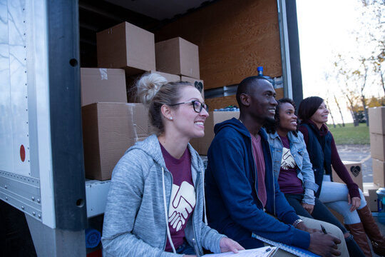 Smiling volunteers sitting at back of truck with cardboard boxes