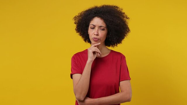 Insighted smart proactive pensive young black woman 20s wears red t-shirt looks around thinks scratches at temple comes up with ideas raised finger isolated on plain yellow background studio portrait