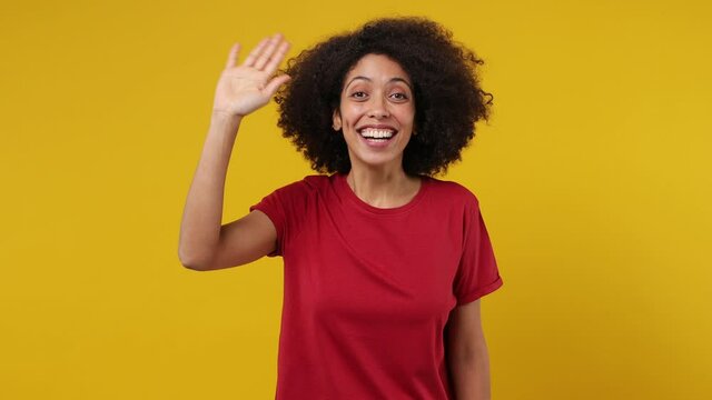 Friendly happy vivid young black woman 20s years old wears red t-shirt look around for friend find waving meet greet with hand as notices someone isolated on plain yellow background studio portrait