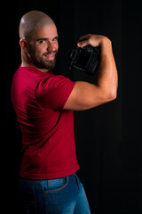 Retrato de homem careca jovem em estúdio com fundo preto. homem vestindo blusa vermelha segurando...
