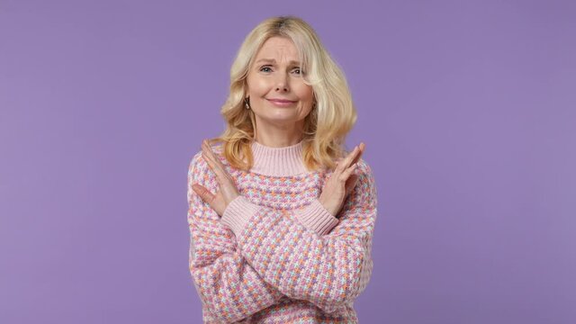 Serious strict severe elderly blonde woman lady 40s years old wears warm shirt say no hold palm folded crossed hands in stop gesture isolated on plain pastel light purple background studio portrait