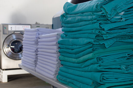 Stack of white sheets and green surgical cloths in an industrial laundry.