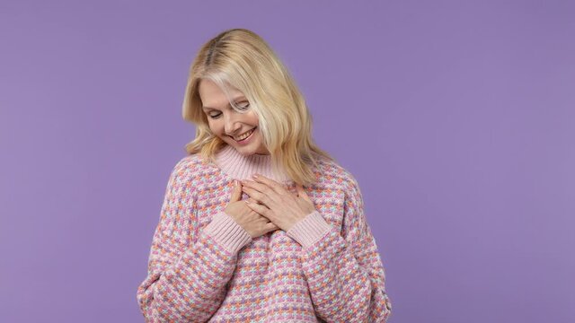 Smiling good kind surprised happy elderly blonde woman lady 40s years old wears warm shirt ask who me oh it so sweet put hands on chest isolated on plain pastel light purple background studio portrait