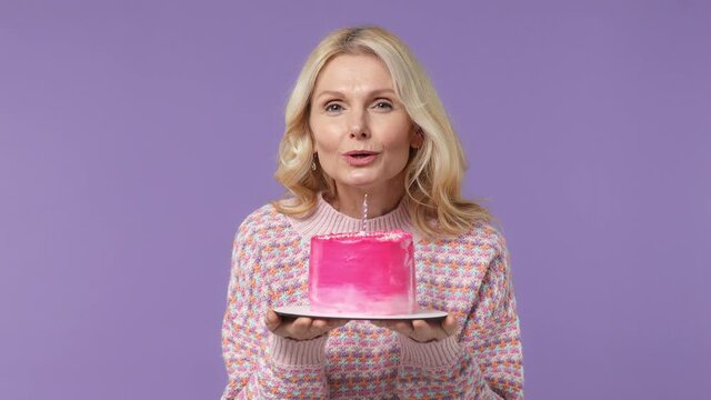 Dreamful happy blithesome vivid elderly blonde woman lady 40s years old wears warm shirt look camera hold birthday cake blow out candle isolated on plain pastel light purple background studio portrait