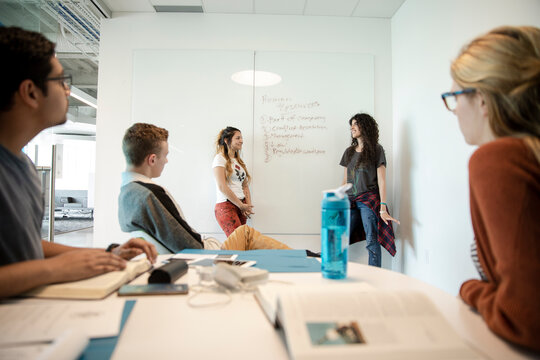 Students discussing in meeting room with young woman presenting