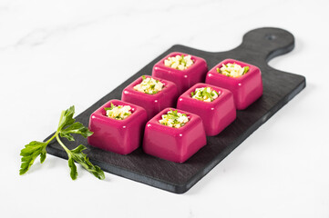 Appetizer beetroot cream jelly in the form of small portions of a square shape with a filling of finely chopped egg with parsley on a serving board on a white background
