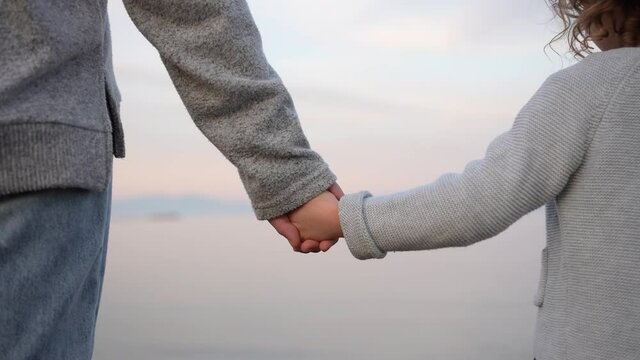  Close up view of the hand of a little girl shaking hands with her older sister on the beach with sea in the background. Concept of love and good relationship between siblings.