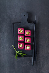 Appetizer beetroot cream jelly in the form of small portions of a square shape with a filling of finely chopped egg with parsley on a serving board on a dark gray background. Top view