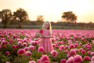 Obraz na płótnie Canvas Little beautiful girl in a peony field on sunset background