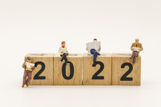 2020 New Year Planning concept. Closeup of group of businessman miniature figure sitting and readng a newspaper or book on stack of wooden number block isolated on white background.