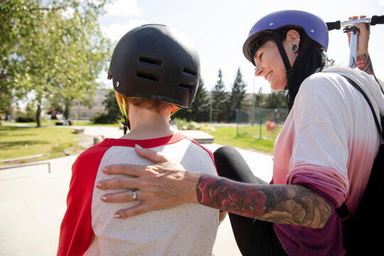 Portrait of happy mother hugging son with skateboard in sunny skate park