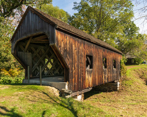 Side view of the Baltimore covered bridge is an old wooden bridge located in Springfield Vermont with dark weathered wood located next to the  Eureka one-room schoolhouse. Summer day in full sun.
