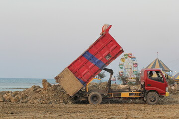 Obraz premium The red truck is unloading its cargo on the beach