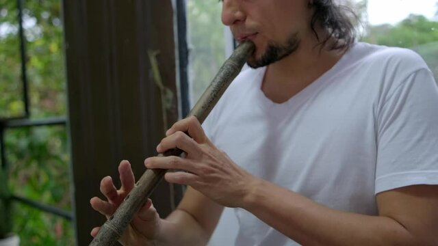 young latin man playing flute made of bamboo in his hands