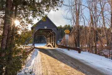 Looking west as the sun gets sets in the west Best's wooden covered bridge in winter located in west Windsor Vermont blue-gray wood stained bridge spanning the mill creek