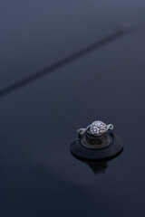 offset round diamond ring against silver with a twisted diamond chip band. Shiny black background....