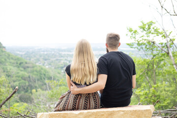 Young couple sitting quietly together overlooking the forest from the mountain. Couple sitting on rock. Cloudy sky in the distance
