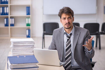 Naklejka premium Young businessman employee and too much work in the office