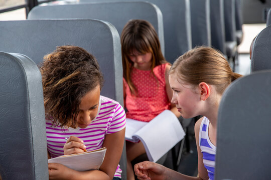 Cute girl looking at friend reading book in bus