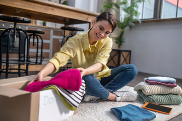 Cheerful female volunteer packing clothes for donation