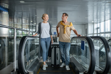 Two middle-aged airport passengers getting off the moving staircase