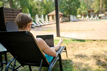 Fototapeta premium A man sitting on a chaise longue and working on a laptop
