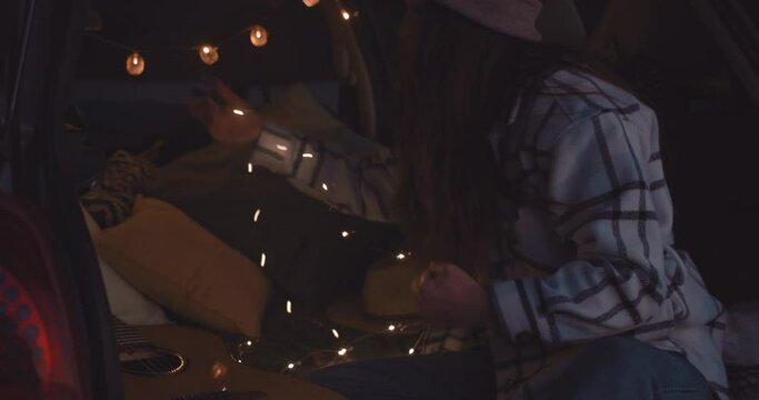 Woman Inside Camper Van Decorating Interior With LED Lights At Night. medium shot