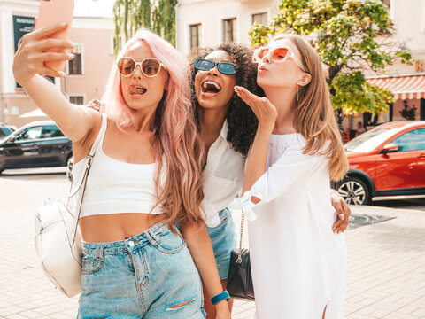Three young beautiful smiling hipster female in trendy summer clothes.Sexy carefree multiracial women posing on the street background.Positive models having fun in sunglasses. Taking selfie photos