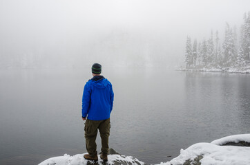 Winter sport activity. An athletic adventurous man standing on the shore of a winter lake surrounded by snow.