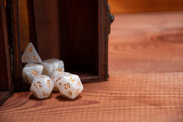 Set of role playing white dices falling out of the storage box on a gaming table made of wood: concept for role-playing games with place for text