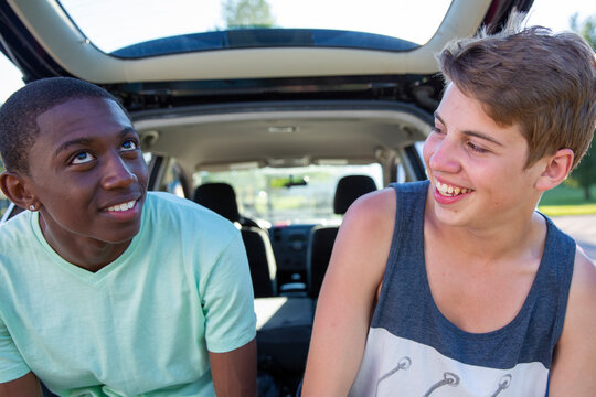 Teens sitting on car bumper