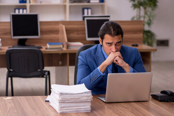 Young male employee and a lot of work in the office