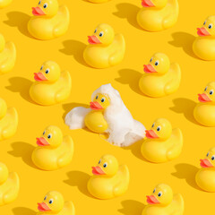 Pattern made with yellow rubber ducks on bright background. One duck in white foam. Positive mood.