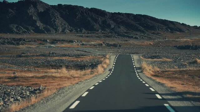 A narrow asphalt road stretched through the outlandish northern landscape. Dark jagged mountains on the horizon. Pan forward, long shot, zoom dolly