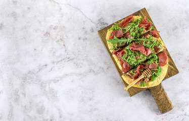 Pinsa Romana or homemade pizza with Italian meat, cheese, figs, arugula, and honey, Sweet savory taste, made from wheat flour, rice flour, and soy flour. Top view, copy space for the recipe.