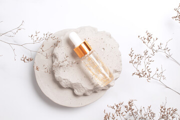 Fototapeta na wymiar Cosmetic serum in glass bottle on stone podium. Natural cosmetic product packaging design, branding. Marble background with flower branch.