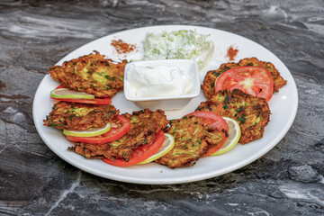 Zucchini hash or Turkish kabak mucver with yoghurt and tomatoes on a white plate