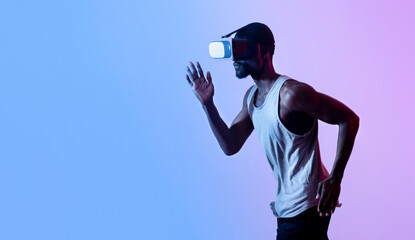 Virtual sports. Young black guy jogging while wearing VR headset in neon light, panorama with free...