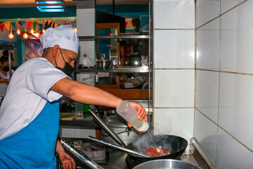 Modern kitchen. Chef pouring ingredients into a wok preparing meals in the restaurant or hotel kitchen. The fire in the kitchen