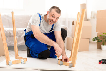 Happy Carpenter Male Assembling Table Smiling To Camera Indoors