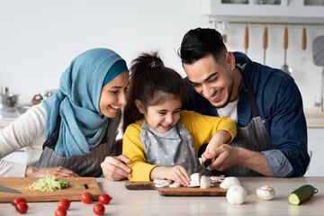 Cheerful Arabic Parents Showing Their Little Daughter How To Cook Healthy Food