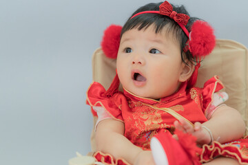 Happy cute infant baby girl in Chinese dress sitting isolated on white background. Cute Asian infant baby sitting in a white living room as concept of Chinese New Year.