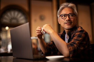 Businessman working on laptop in cafe. Handsome senior man enjoying in fresh coffee