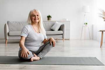 Mature woman exercising at home on yoga mat, posing